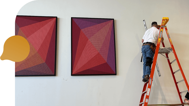 A man is using a ladder to reach and paint a large artwork, demonstrating skill and concentration.