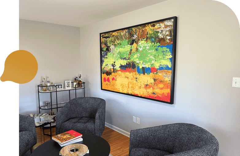 A cozy living room featuring a colorful painting hanging on the wall, with comfortable furniture arranged around the space.