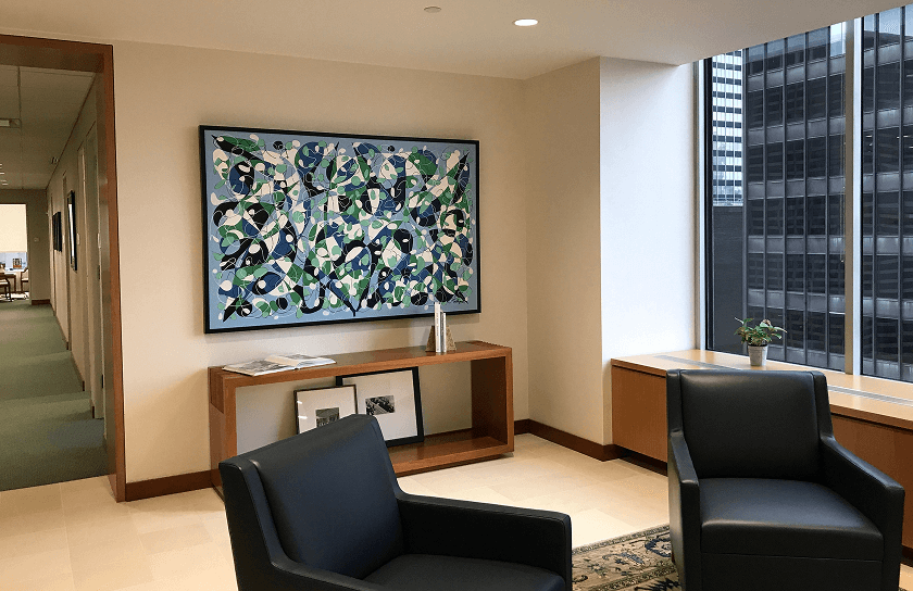 An office waiting area with two black leather chairs, a wooden console table, and a large abstract painting in blue, green, and white hanging above it. A skyscraper window is on the right.