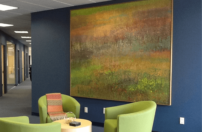 A painting of a vibrant field displayed in an office, complemented by modern green chairs arranged around it.